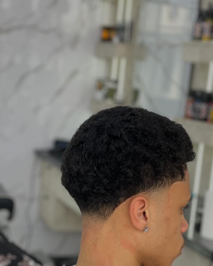 The back and side of a tight curly cut, tapered short into the neck and around the ear