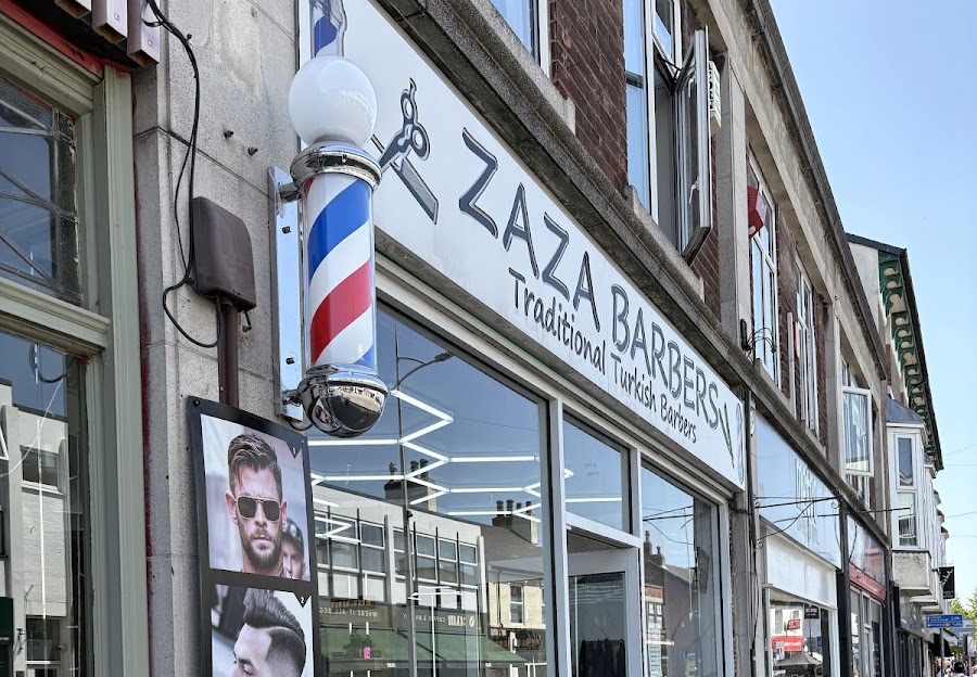 The Zaza Barbers fascia at 118 High Road, signwritten in black capitals with the words Traditional Turkish Barbers beneath, and a red, white and blue barber pole mounted beside it