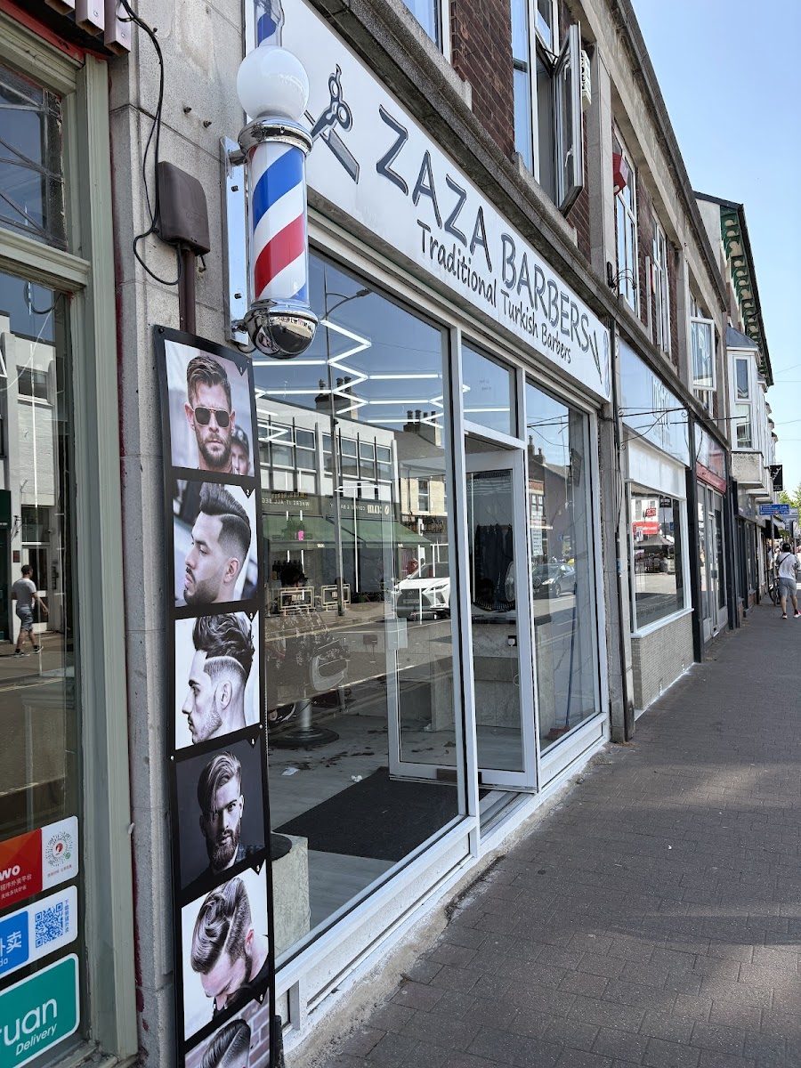 The Zaza Barbers shopfront seen from the pavement, with the barber pole, the fascia and the boards of haircut photographs in the window